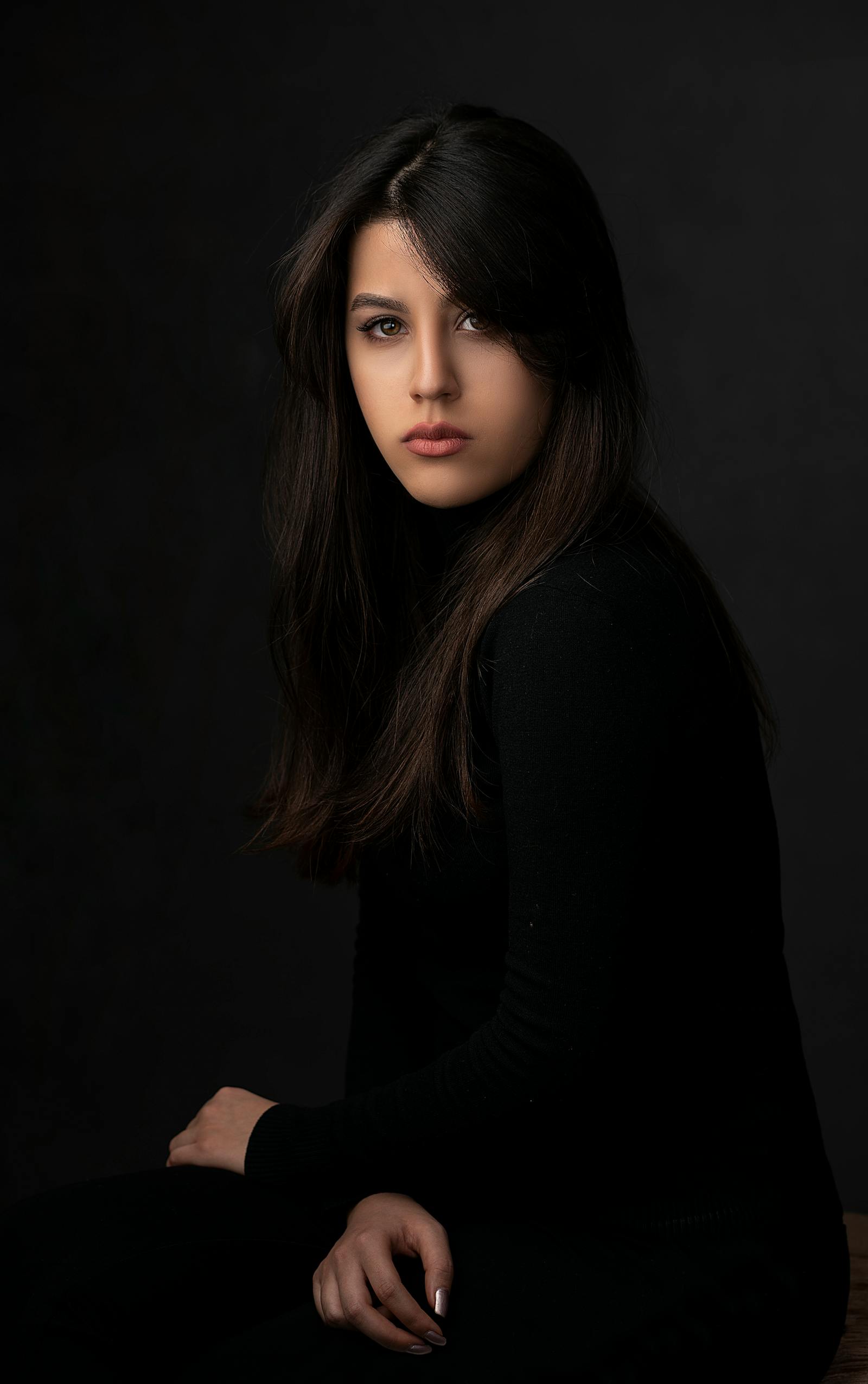 A studio portrait lit in warm tungsten — a young woman in profile against a deep charcoal seamless, soft fall-off on her shoulder, signature Lumina Studio lighting.