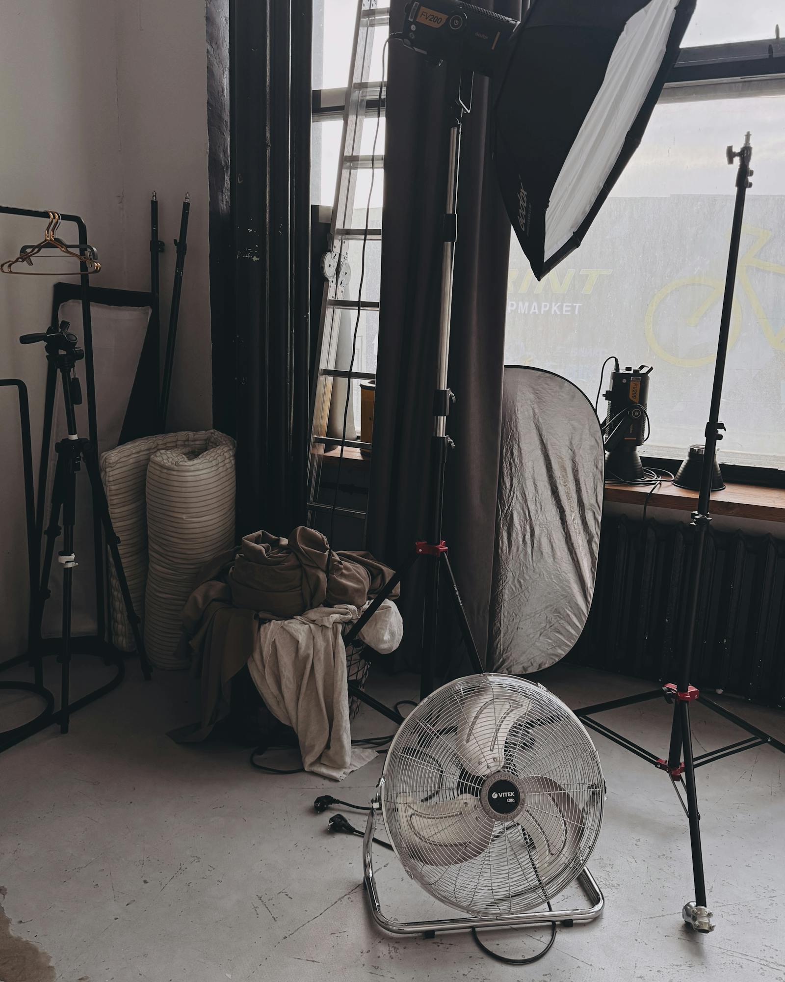 The Brooklyn studio with a tall north window, a rolled grey seamless, and two stylists steaming a garment on a rolling rack.